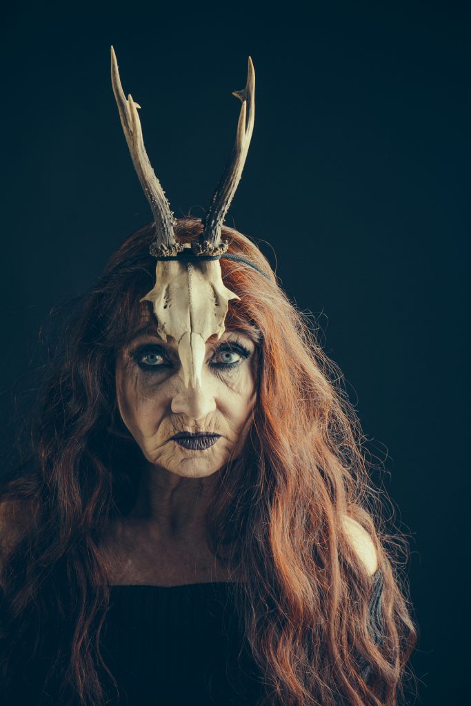 Halloween old lady with candle and antler. Halloween woman in black with long red hair and makeup. traditional party. holiday celebration. old woman on black background.