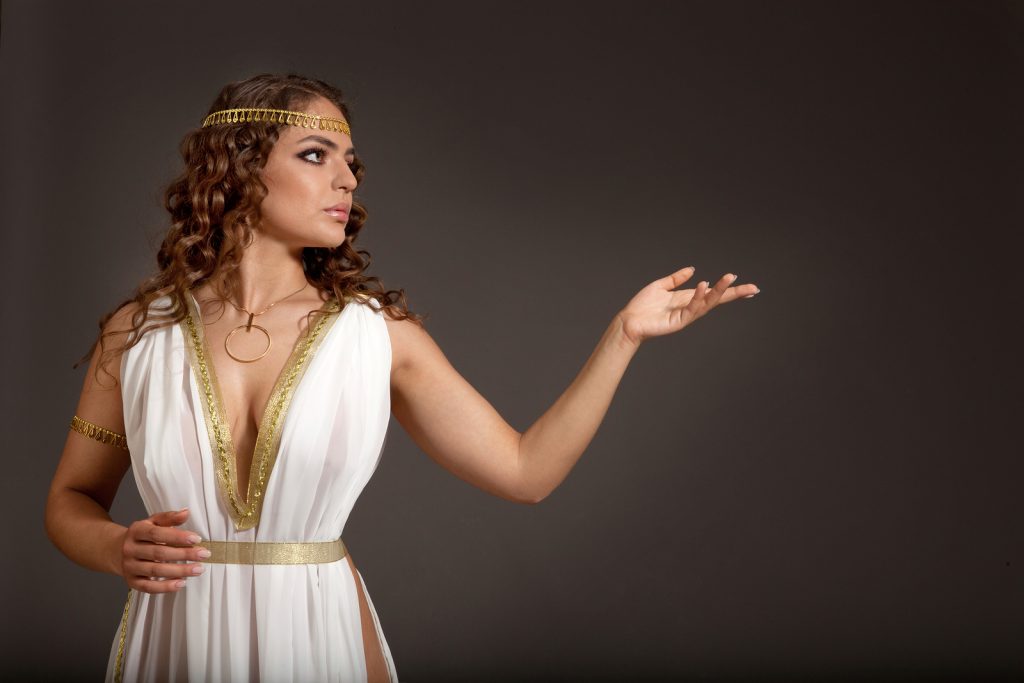 The Beautiful Young Woman Wearing White and Gold Greek Costume Looking to Something on her Left on the Dark Background
